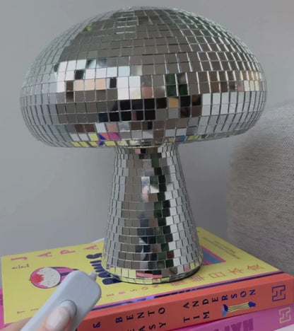 Disco mushroom lamp on books with a hand holding the remote control