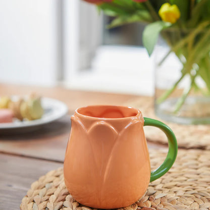 Orange Tulip mug on a table with a vase of flowers in the background