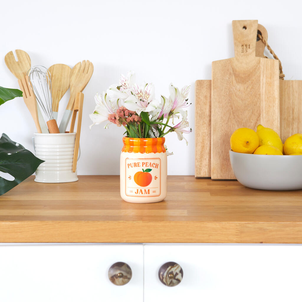 Jam vase, peach version with pink flowers, on a worktop between chopping boards and lemons
