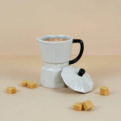 Grey Moka Mug full of coffee on a beige background, lid resting beside it