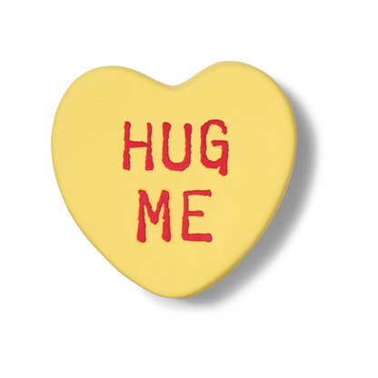 Hug Me heart-shaped box in yellow, closed, front view with the red lettering.