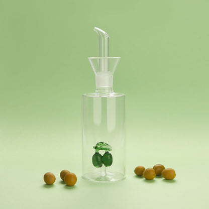 Olive oil cruet in clear glass with the olive decoration at the base, green background