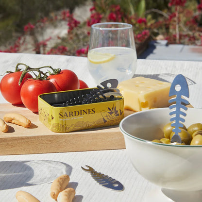 Conserverie Sardines forks on a table with tomatoes, cheese, olives and the open yellow tin.