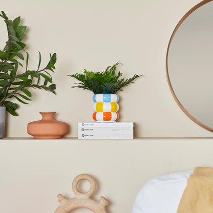 Float flower vase with a fern on a shelf, next to a round mirror