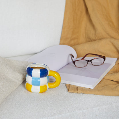 Floats Gialla mug resting on a sofa next to an open book and a pair of glasses