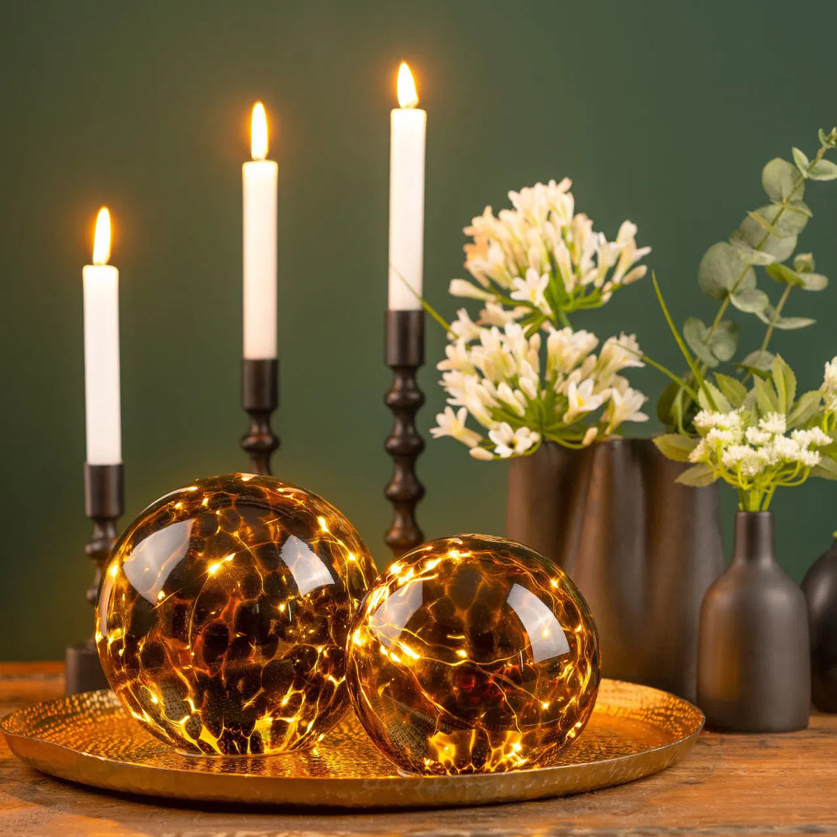 Totem candle holder, two illuminated glass spheres on a golden tray next to lit candles.