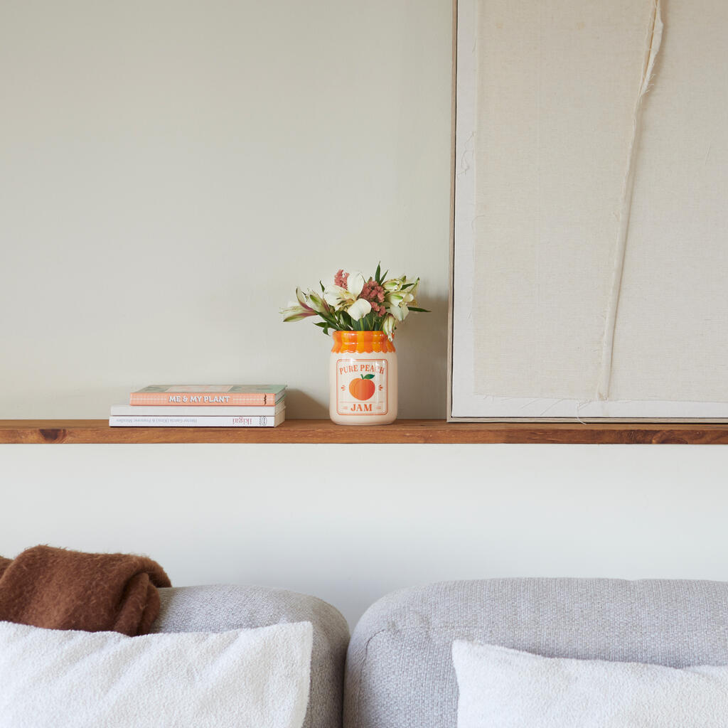 Jam vase, peach version on a wooden shelf, under a painting and above a grey sofa