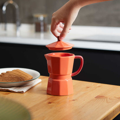 Orange Moka mug on a wooden table with biscuits, lid resting beside it