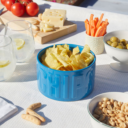 Ciotola Snack Chips azzurra su una tavola apparecchiata con pomodori, formaggio, carote e olive