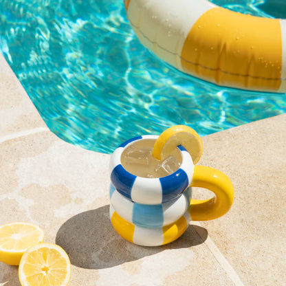 Floats Gialla mug poolside with a lemon slice on the rim and a pool float behind it