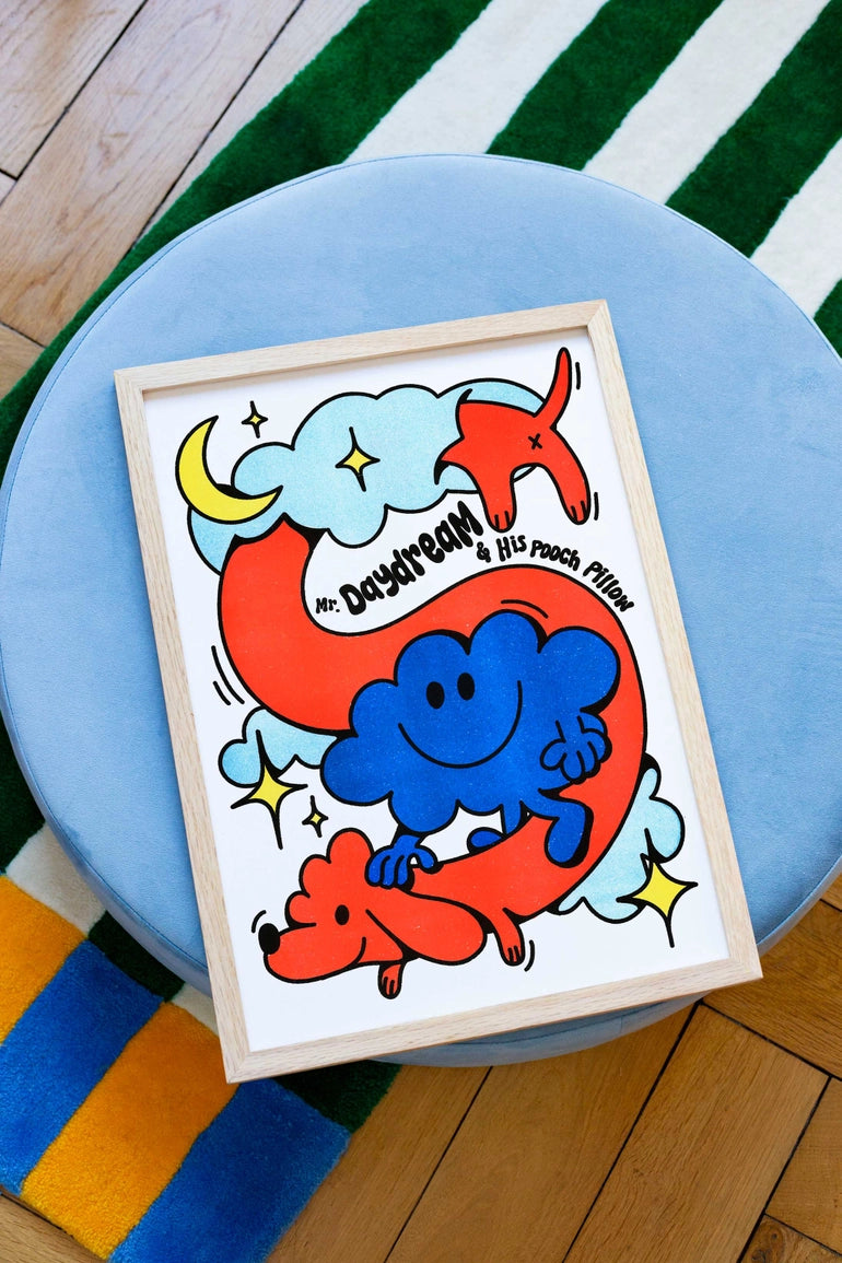 The 'Mr. Daydream' print leaning against a blue pouf, with a colourful striped rug in the background.