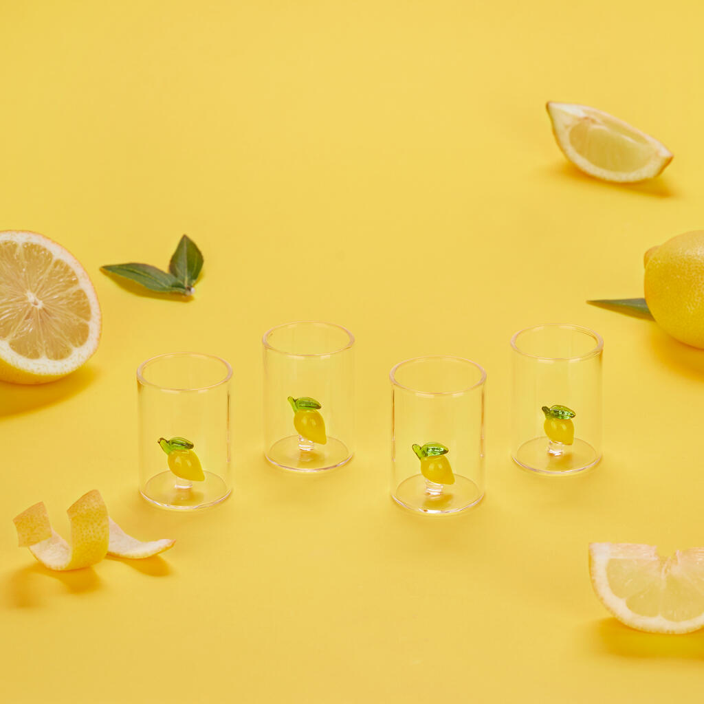 Lemon liqueur glasses on a yellow background, surrounded by real lemons and peel