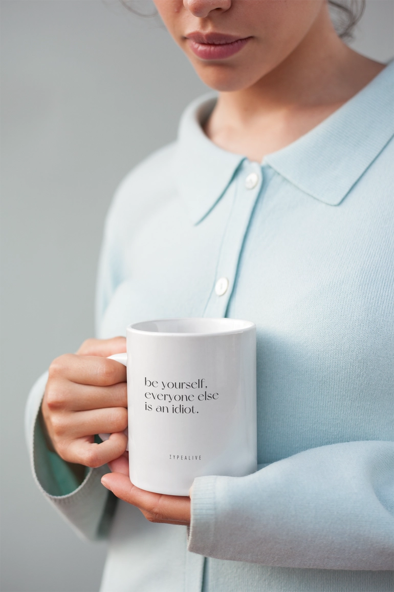 Be Yourself mug in white, held by a person wearing a light blue cardigan.