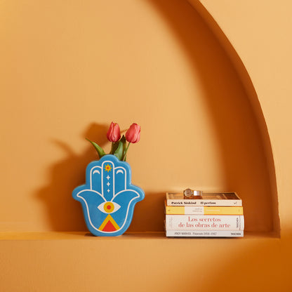 Blue Lucky Hand vase with pink tulips on a shelf next to some books