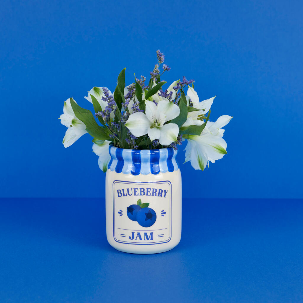 Jam vase, blueberry version with white and lavender flowers, surrounded by blueberries on blue