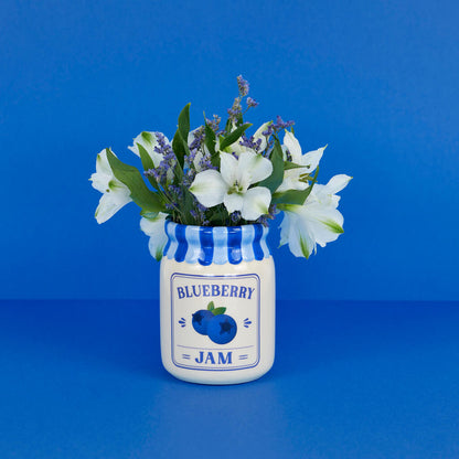 Jam vase, blueberry version with white and lavender flowers, surrounded by blueberries on blue