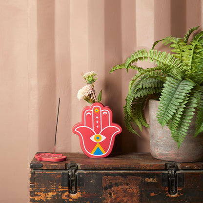 Red Lucky Hand vase with white flowers on a wooden trunk