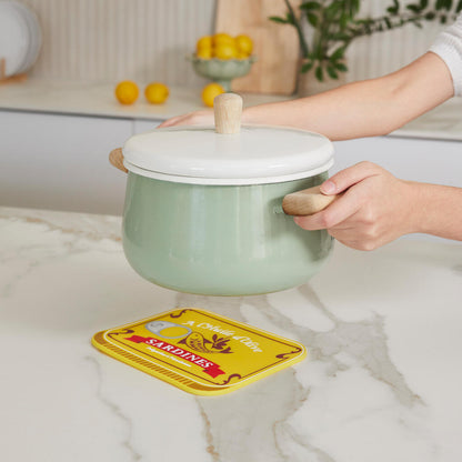 Sardines Trivet: a hand placing the green pot with lid on top of the sardine-print trivet.