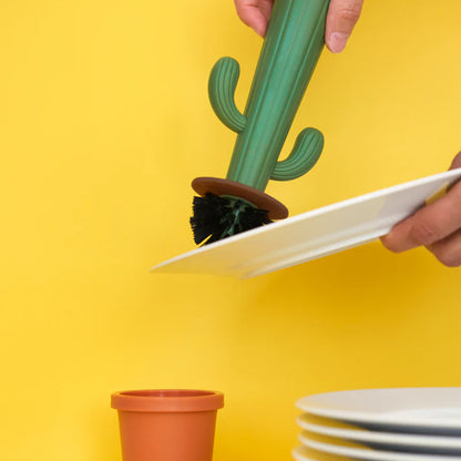 Cactus dish brush held in hand while scrubbing a white plate.